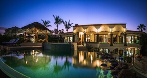 Um resort com piscina, palmeiras e um prédio com telhado de palha.