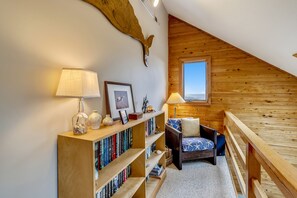 Eine gemütliche Leseecke mit Bücherregal aus Holz, einer Lampe und einem Sessel mit Blick ins Freie.