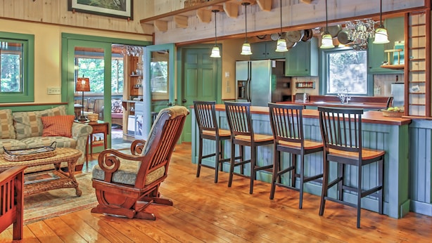 Un intérieur rustique avec des planchers en bois, un coin repas doté de tabourets de bar, un fauteuil à bascule et un espace cuisine équipé d’un réfrigérateur et d’un évier.