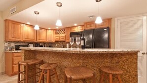 A kitchen with wooden cabinets, a granite countertop, a black refrigerator, and three bar stools.