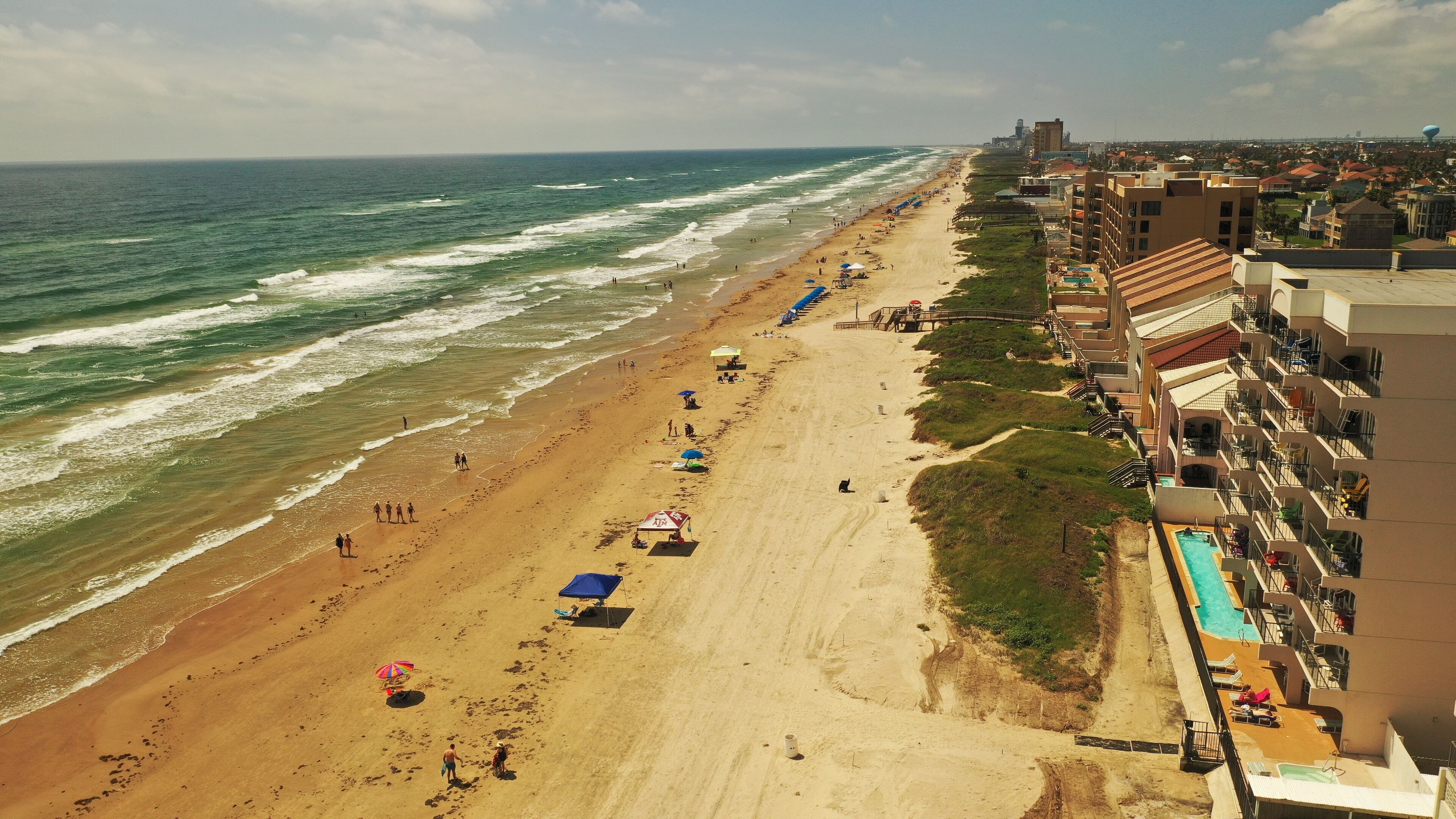 Een strand met een lange zandvlakte, een zwembadgedeelte en gebouwen aan de kust.