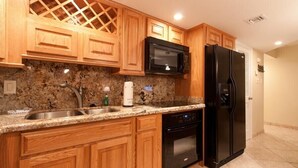 A kitchen with wooden cabinets, a granite countertop, a black microwave, a black refrigerator, and a stainless steel sink.