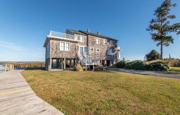 A two-story wooden house with a balcony, a wooden deck, and a grassy yard.