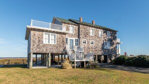 A two-story wooden house with a balcony, a covered porch, and a view of the beach.