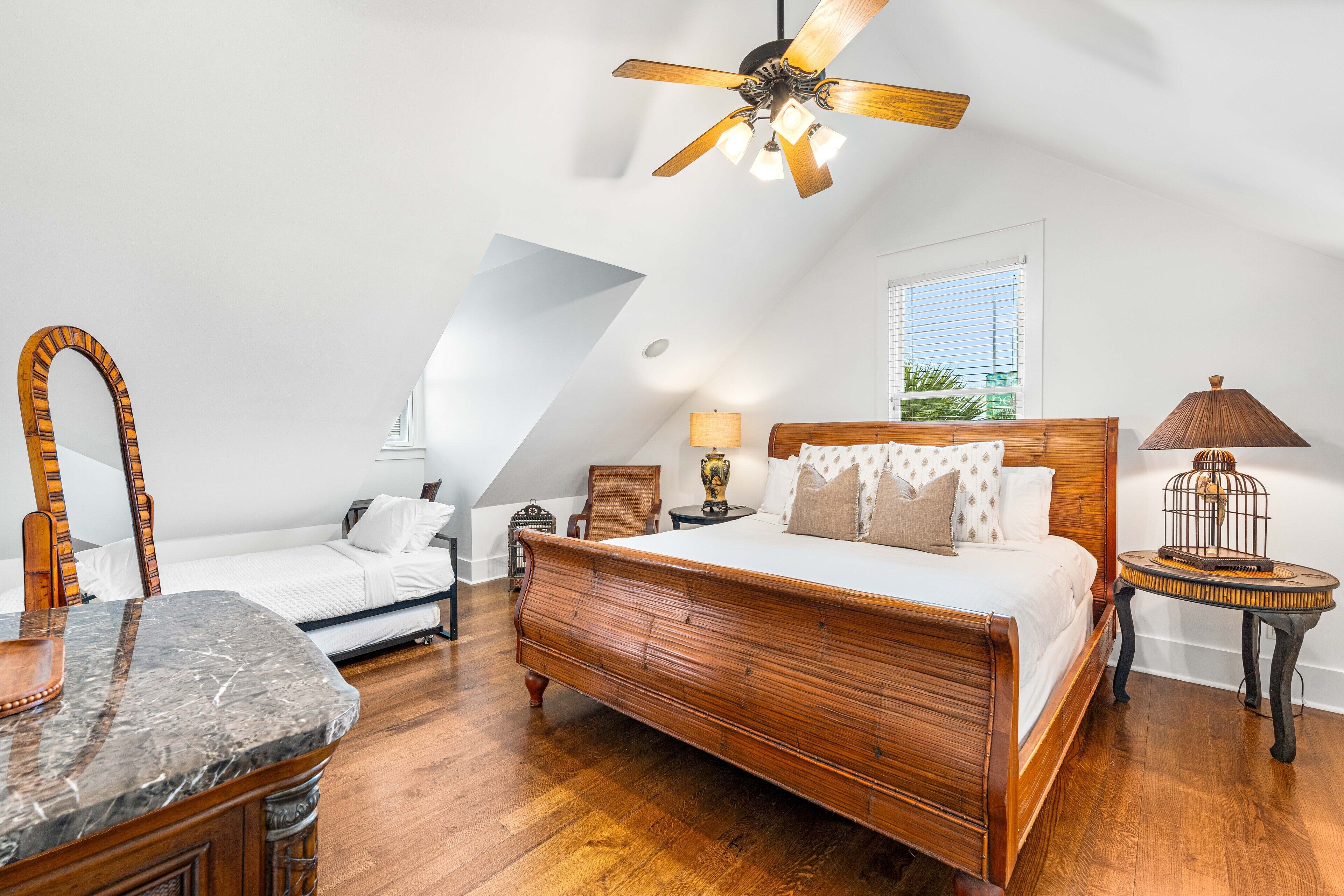 A bedroom with a wooden bed, a desk, a chair, a ceiling fan, and a window with blinds.