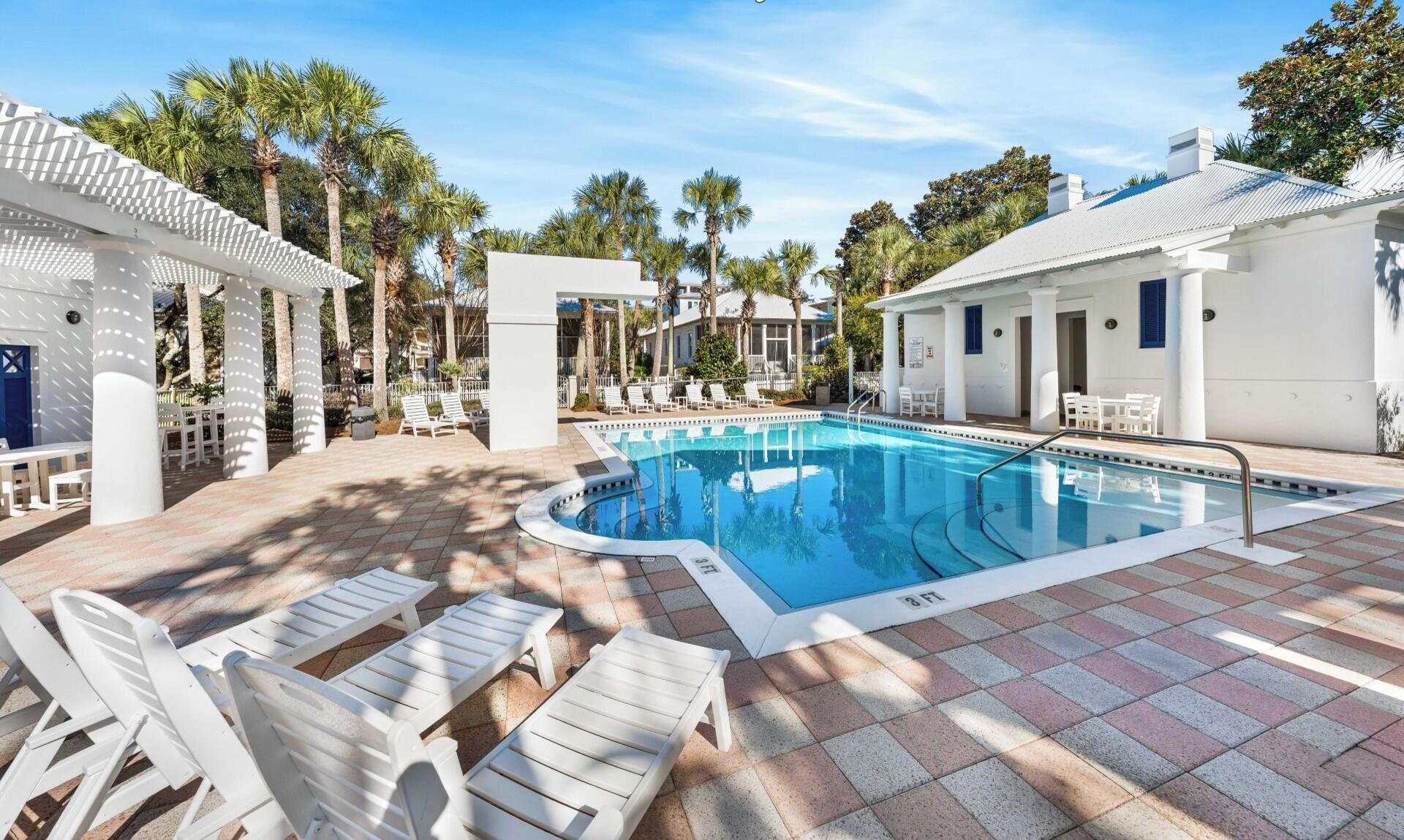 A swimming pool with lounge chairs, a covered seating area, and palm trees in the background.