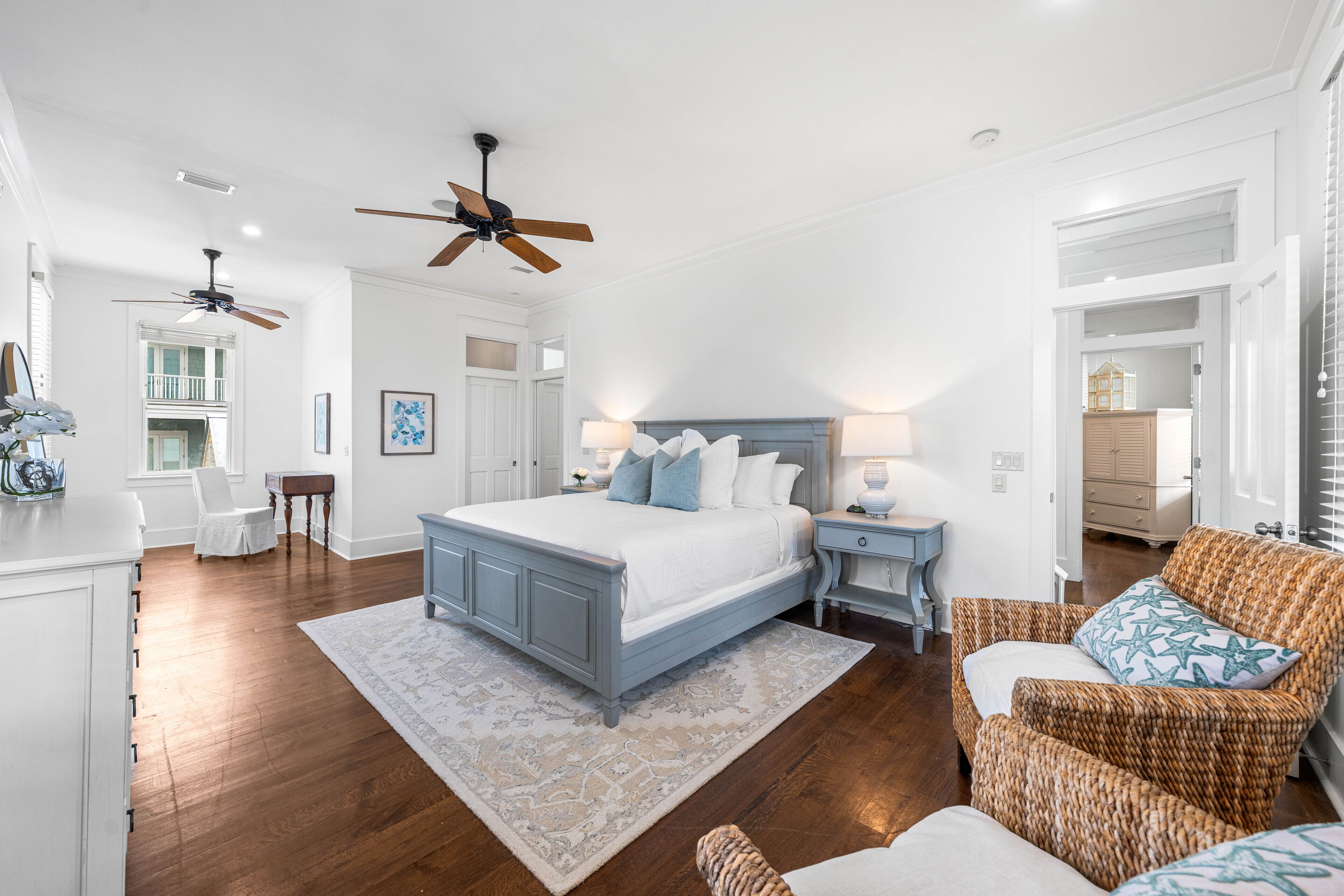 A spacious bedroom with a large bed, two nightstands, a wicker armchair, and a ceiling fan.