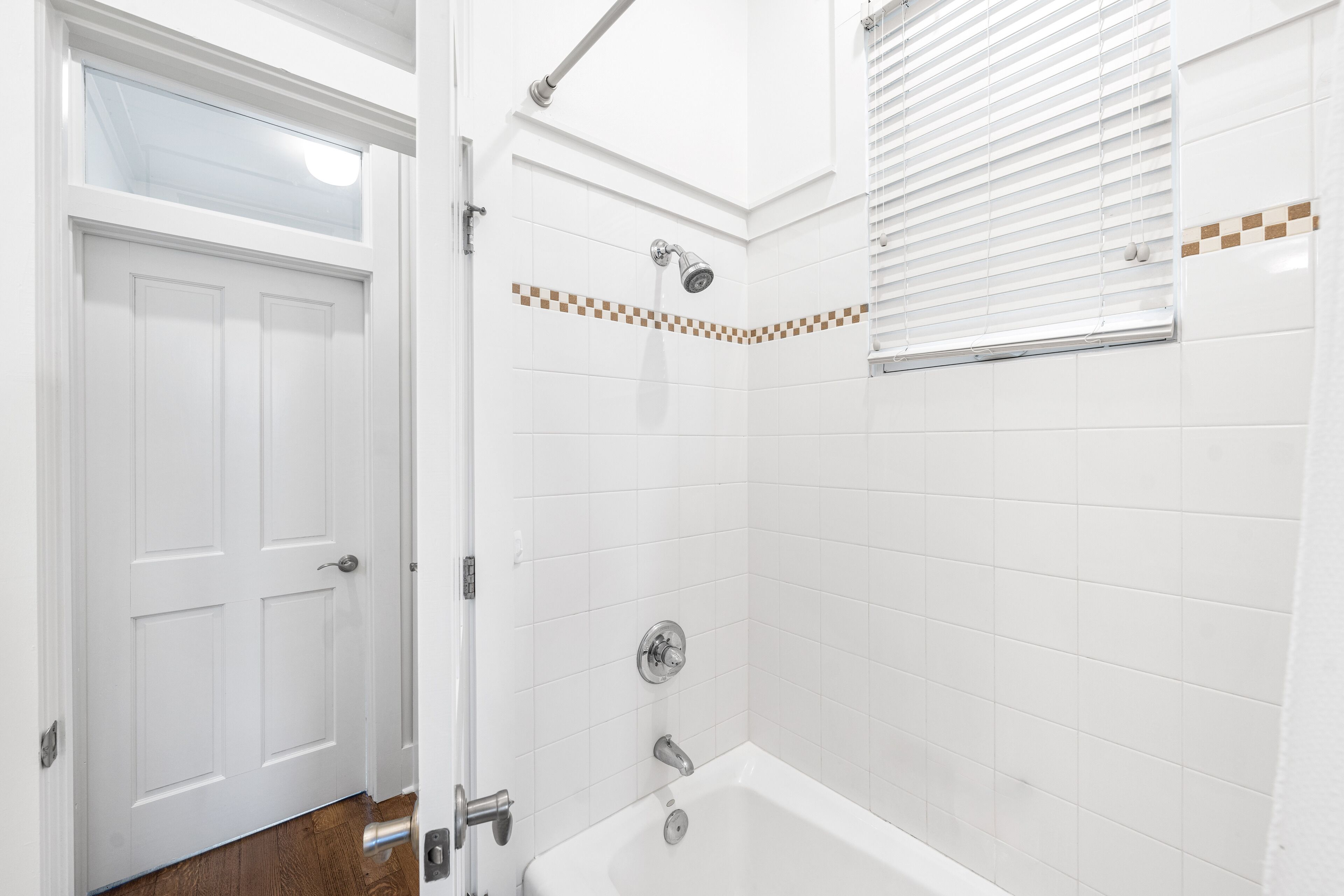 A bathroom with a white door, a shower with a handheld showerhead, and a bathtub.