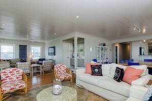 A spacious living room with a white sofa, patterned chairs, a coffee table, and a dining area with blue chairs.