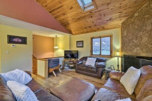 Un salón acogedor con techo de madera, chimenea de piedra y televisor.