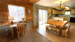 A cabin interior with a wooden dining table, chairs, a chandelier, and a kitchen area. - Loose Moose @ Spring Brook Resort (Wisconsin Dells)