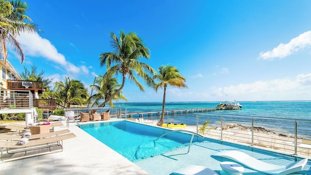 A pool area with lounge chairs, palm trees, and a view of the ocean. - Blue Serenity: Beach House w/Pool, Pickleball Courts + Backyard Snorkeling (Grand Cayman)