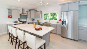 A modern kitchen with a large island, stainless steel appliances, and light gray cabinetry. - Blue Serenity: Beach House w/Pool, Pickleball Courts + Backyard Snorkeling (Grand Cayman)