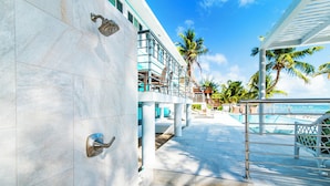 A modern hotel exterior with a pool area, palm trees, and a clear sky. - Blue Serenity: Beach House w/Pool, Pickleball Courts + Backyard Snorkeling (Grand Cayman)