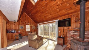 Ein Holzblockhaus-Interieur mit einer Couch, einem Fernseher, einem Kamin und einer Küchenzeile.