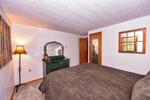 A bedroom with a bed, dresser, mirror, lamp, and a window.