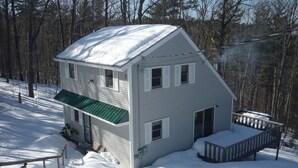 Ein zweistöckiges Haus mit einem grünen Dach, einer Veranda und einer mit Schnee bedeckten Terrasse.
