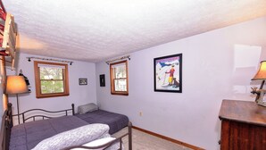 Ein Schlafzimmer mit zwei Betten, einer hölzernen Kommode, einem Fenster und einem Poster an der Wand.