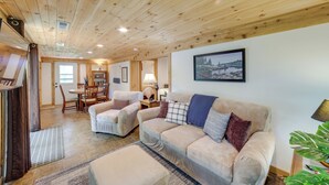 Un salon chaleureux avec un plafond en bois, un canapé beige, une table basse et un coin repas comprenant des chaises et une table.