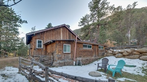 A rustic log cabin with a stone foundation, a wooden porch, and a snow-covered ground. - Rustic Log Cabin w/ Studio ~ 5 Mi to Pikes Peak! (Green Mountain Falls)