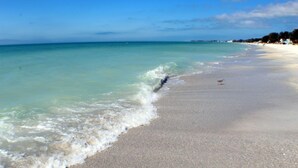 A beach with clear water, a sandy shore, and a distant shoreline with buildings. - LAST MINUTE DEAL, Charming Elevated Duplex – Relaxing Beach Getaway Near Anna Maria Island- Bay access (Bradenton)