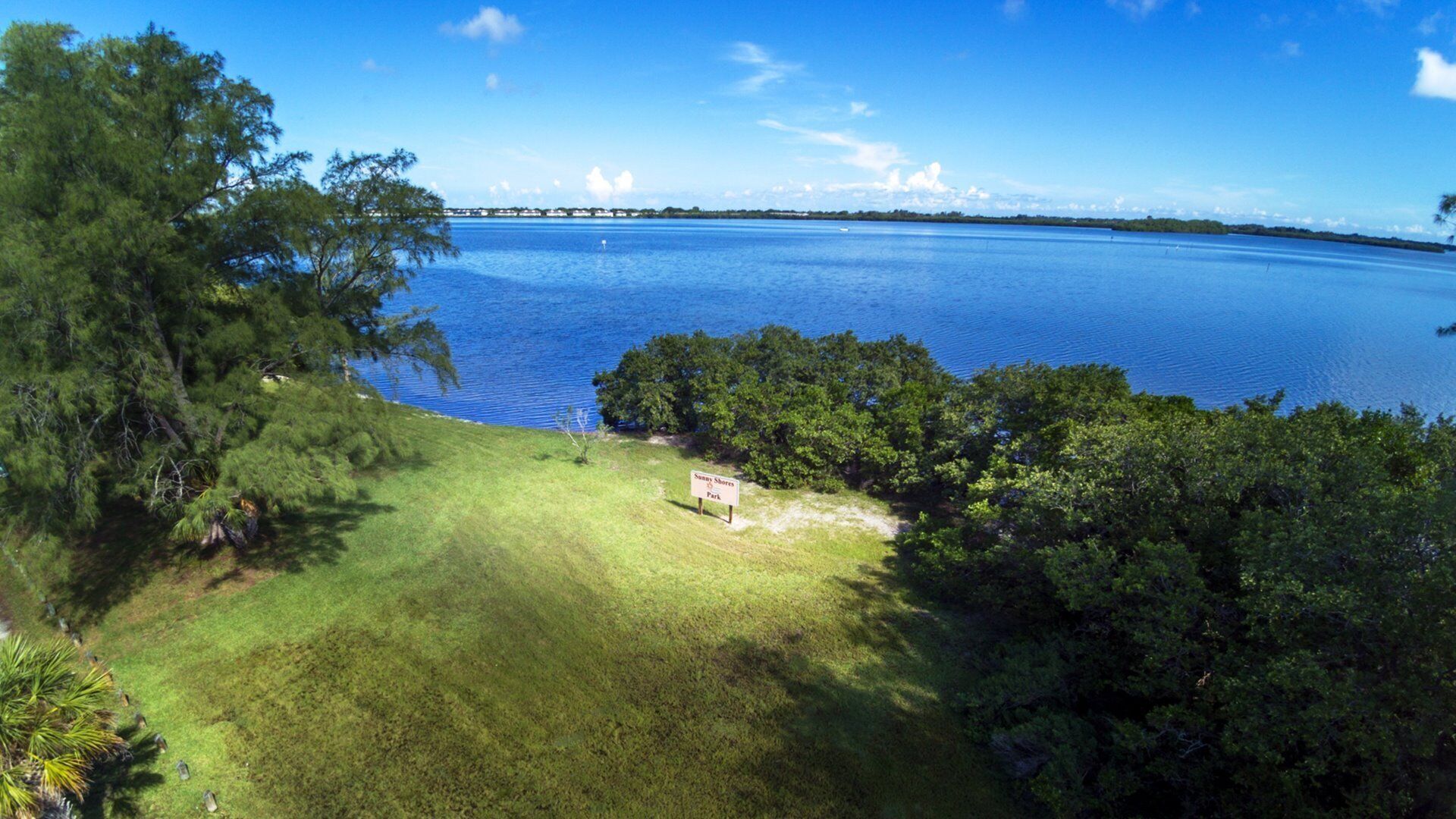 A park with a sign reading "Sunny Shores Park" surrounded by trees and a large body of water.