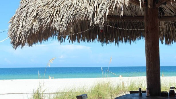 A beachside restaurant with a thatched roof, wooden tables, and chairs, overlooking a sandy beach and the ocean. - LAST MINUTE DEAL, Charming Elevated Duplex – Relaxing Beach Getaway Near Anna Maria Island- Bay access (Bradenton)
