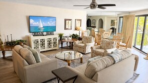 A spacious living room with a large TV, comfortable seating, and a view to the dining area.