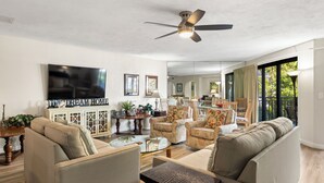 A spacious living room with a flat-screen TV, comfortable seating, a ceiling fan, and a view of the outdoors through large windows. - Mar Y Sol –Luxurious oceanfront  Key West Breathtaking Atlantic Sunrise Views (Key West)