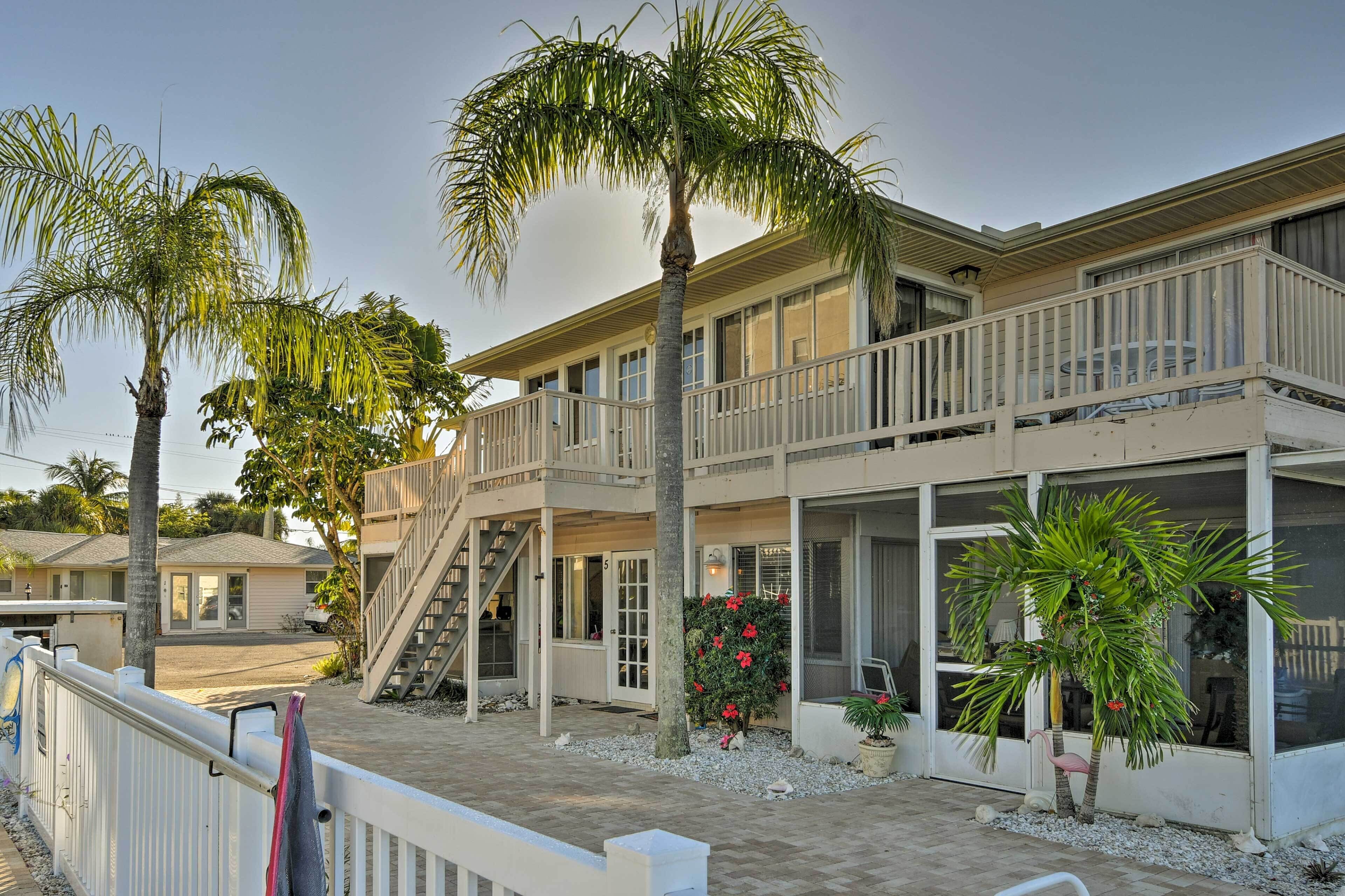 A two-story building with a balcony, palm trees, and a small garden area.