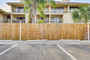 Un edificio de dos pisos con cerca de madera, estacionamiento y una palmera.