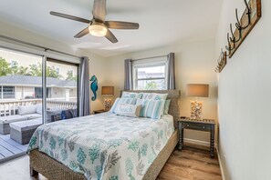 Un dormitorio con cama, ventilador de techo, mesita de noche, lámpara y vistas al exterior.