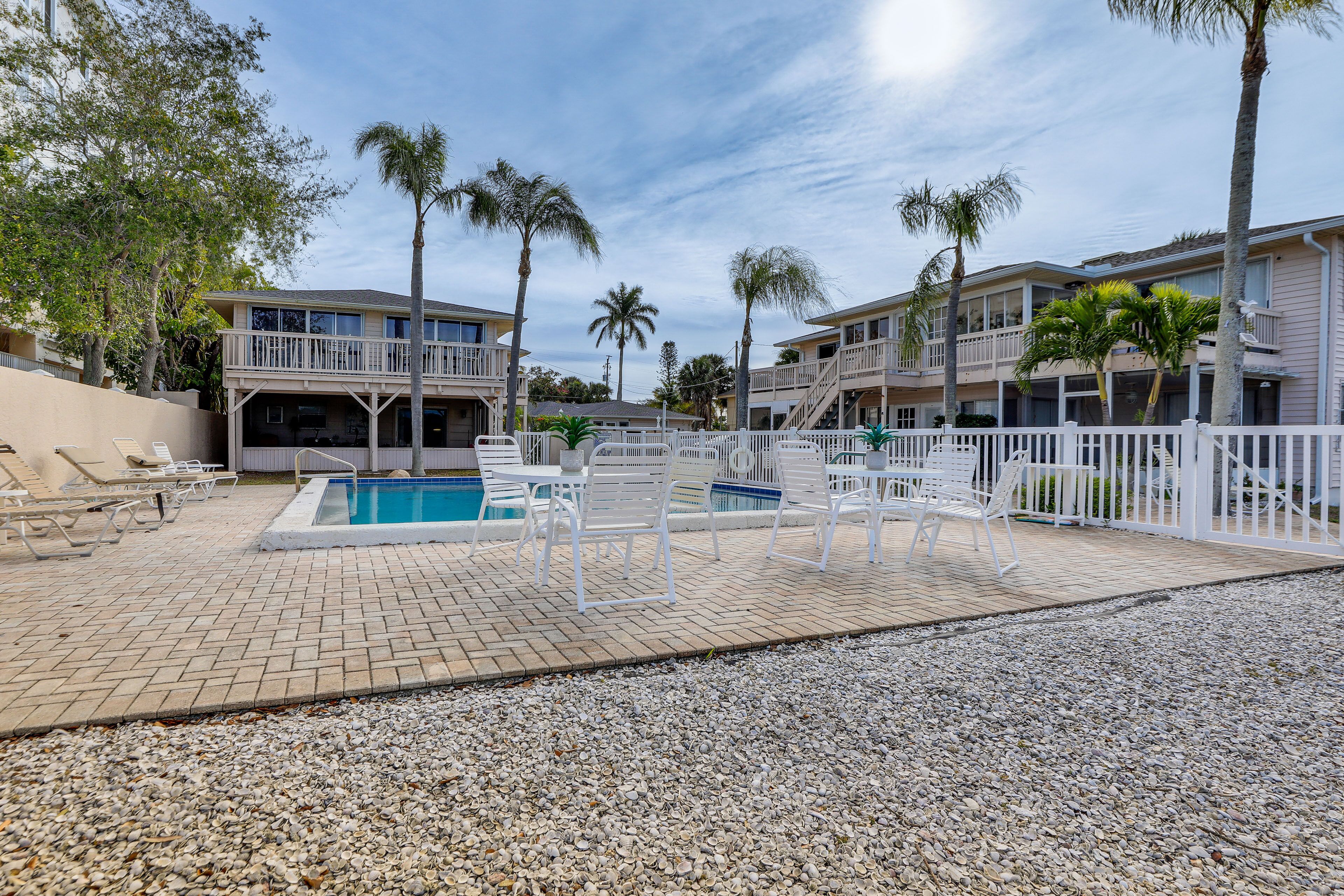 A pool area with lounge chairs and a pool, surrounded by palm trees and a building with balconies.