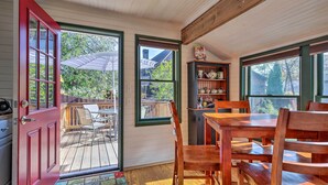 A cozy room with a wooden table and chairs, a red door, and a view of a deck and trees outside. - Walk to Lake George! Bolton Landing Cottage (Bolton Landing)