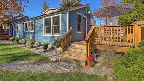 A blue house with a red door, wooden steps, and a deck with a striped umbrella. - Walk to Lake George! Bolton Landing Cottage (Bolton Landing)