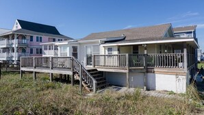 Una casa sulla spiaggia con una veranda in legno, una scala che conduce all'ingresso e una vista libera sull'oceano.