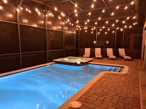 An indoor swimming pool with a hot tub, surrounded by lounge chairs and string lights. - 8BR ChampionsGate Villa | Theater & Themed Rooms (Davenport)