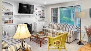 A modern living room with a sofa, armchairs, a glass coffee table, and a TV mounted on the wall. - The Heron's Nest - Sea Breezes & Sweet Dreams (Chatham)