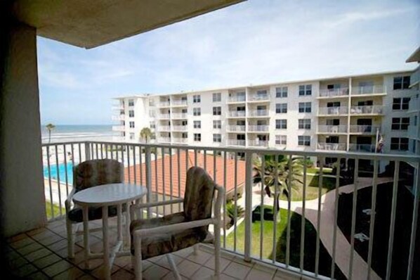A balcony with a table and chairs, overlooking a pool and a building with multiple balconies.