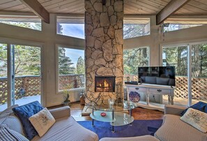 Cozy living area with a stone fireplace, comfortable sofa, and large windows offering views of the surrounding trees.