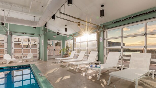 Un espace piscine doté de chaises longues baignées de soleil et offrant une vue dégagée sur le coucher du soleil à travers de grandes fenêtres.