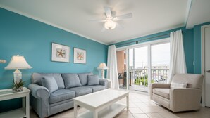 Un salon avec un mur bleu, un canapé gris, une table basse blanche, un fauteuil beige et un ventilateur de plafond.