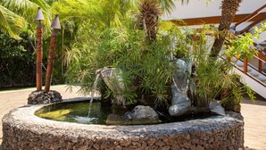 A circular stone fountain with water, surrounded by tropical plants and palm trees. - Aloha Aku Ohana Suite – Spacious Garden View Oasis (Kihei)