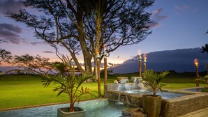 A serene outdoor pool area with a waterfall, surrounded by tropical plants and a large tree. - Aloha Aku Ohana Suite – Spacious Garden View Oasis (Kihei)