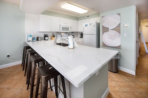 A kitchen with white cabinets, a large island with bar stools, a microwave, and a refrigerator.