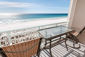 Een balkon met een tafel en stoelen, met uitzicht op een strand.