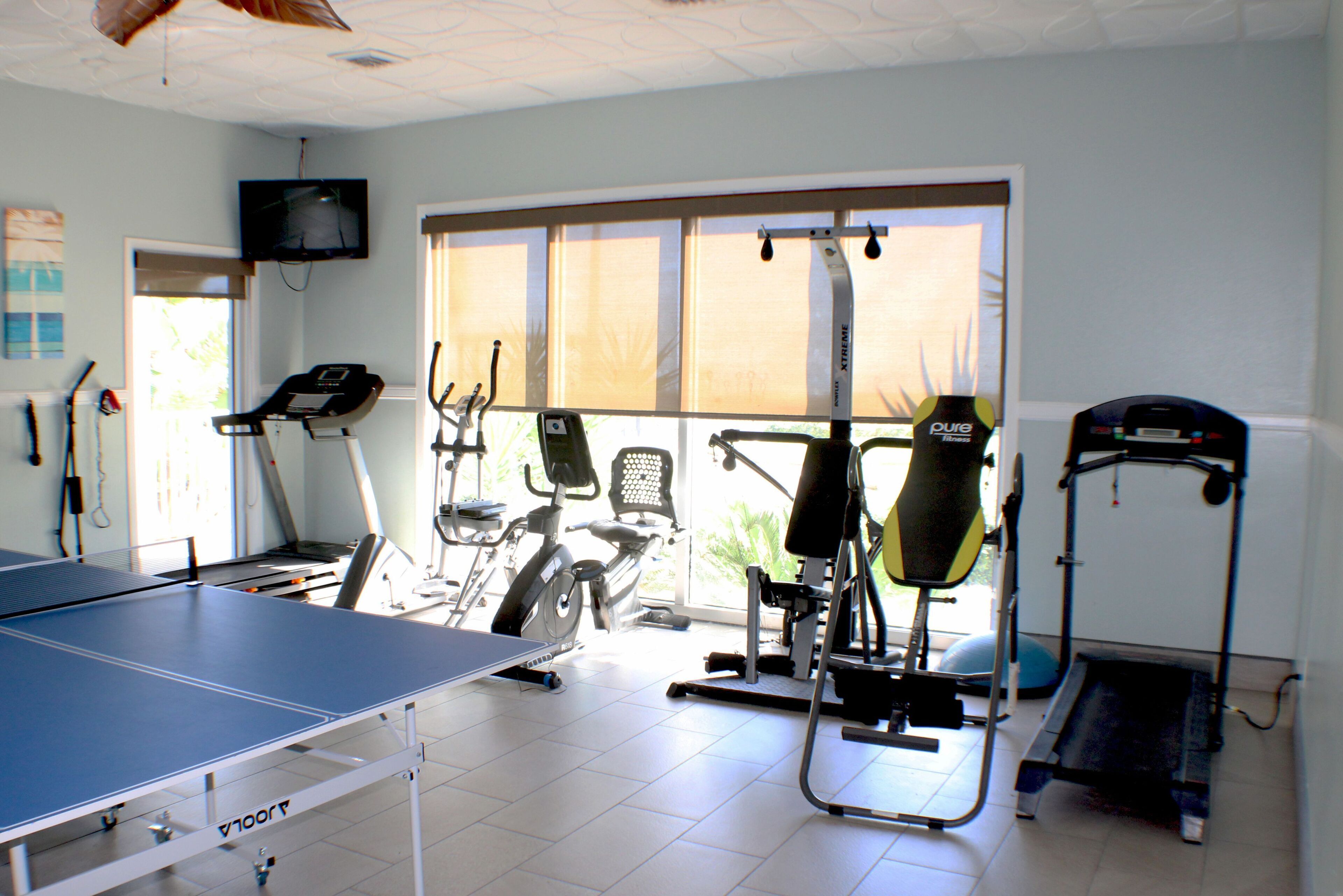Een fitnessruimte met trainingsapparatuur, een tafeltennistafel en een aan de muur bevestigde televisie.
