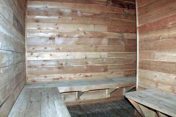 Interior de una cabaña de madera con un banco y piso de madera.