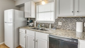 A kitchen with white cabinets, a granite countertop, a built-in dishwasher, a window with blinds, and a paper towel dispenser. - Walk to Gulf: Surfside Beach Home w/ Deck (Surfside Beach)