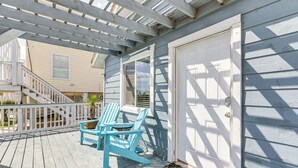 A wooden deck with two blue Adirondack chairs, a white door, and a staircase leading to an upper level. - Walk to Gulf: Surfside Beach Home w/ Deck (Surfside Beach)